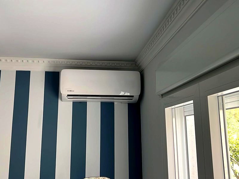 Split MundoClima sobre pared a rayas azul en dormitorio de villa